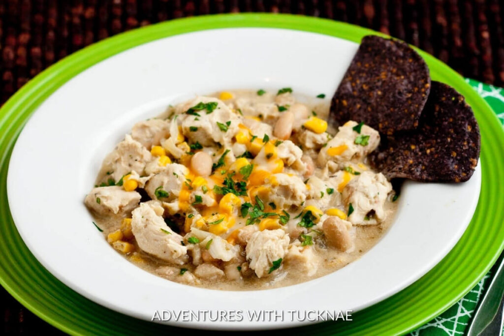 Crockpot White Bean Chicken Chili featuring shredded chicken, white beans, and corn in a creamy sauce, garnished with cheese and fresh parsley.