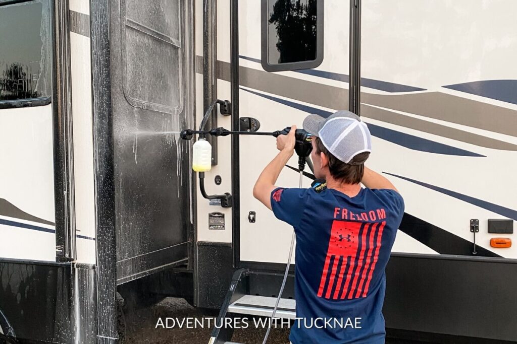 A man using a pressure washed on the exterior of a modern RV, illustrating an RV gift idea.