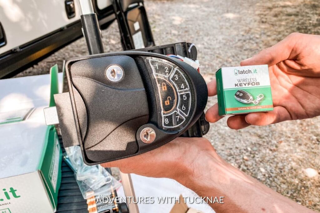 A person's hand holding a wireless key fob next to an RV lock, highlighting a convenient and secure gadget gift for RV owners for easy access.