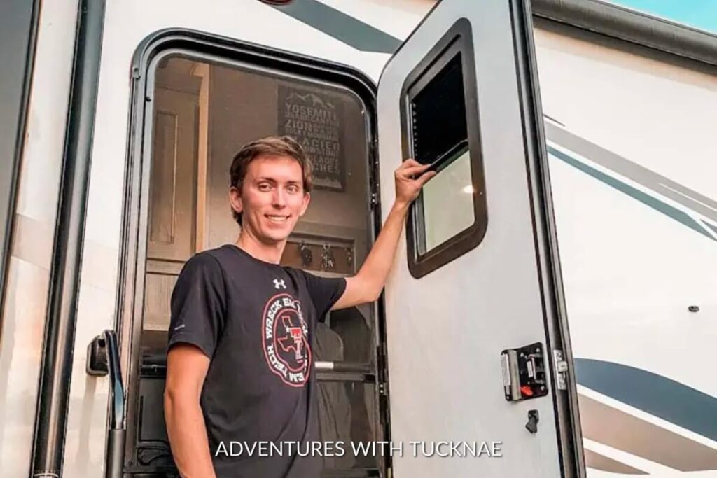 A man in a casual outfit smiling while using an electronic control panel on an RV, representing a high-tech gift idea for RV enthusiasts for streamlined operation.