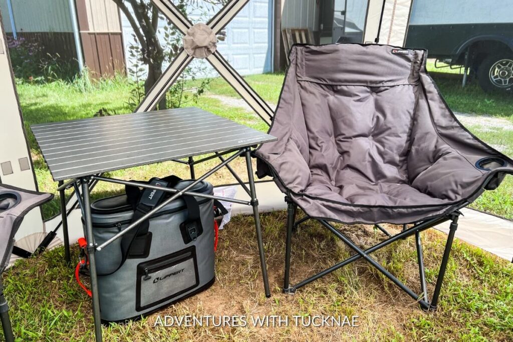 An array of RV camping accessories displayed outdoors, including a collapsible chair and table, and a portable cooler, showcasing practical gift options for RV travelers.