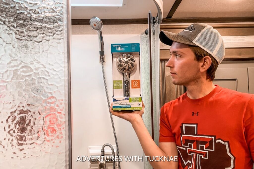 A man comparing a new showerhead with the one installed in an RV bathroom, suggesting upgrades as thoughtful gifts for RV owners.