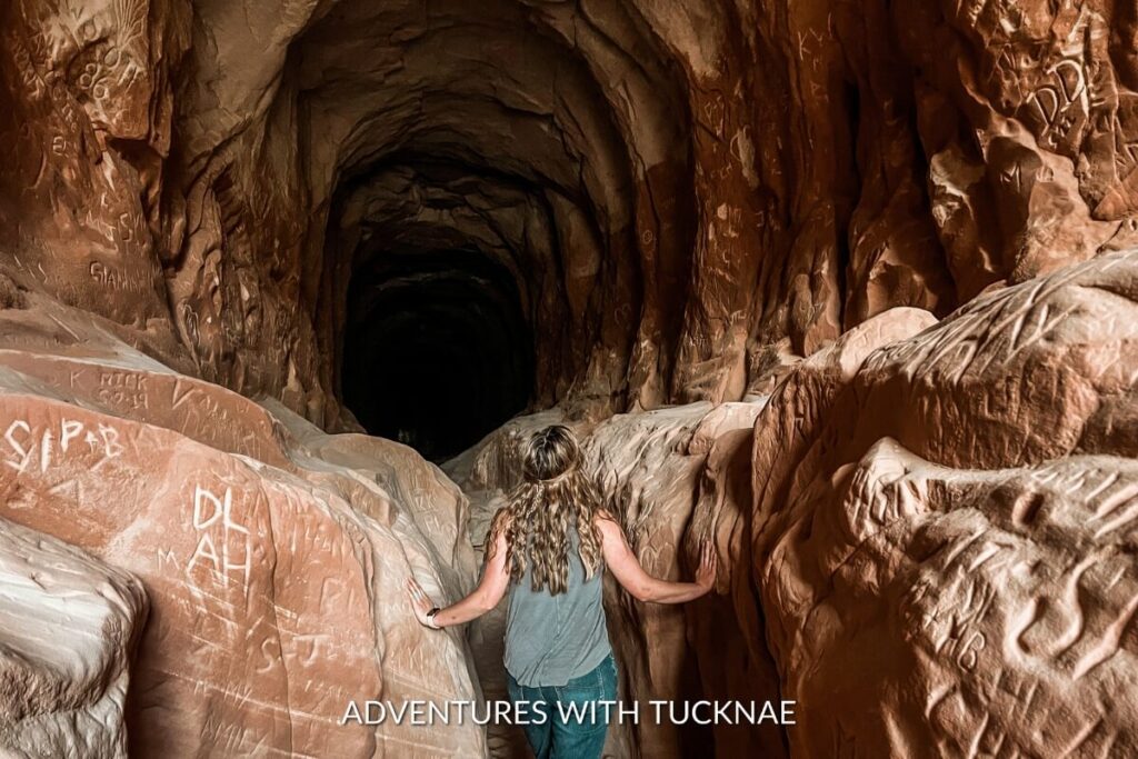 An explorer touches the rugged walls of Belly of the Dragon, a captivating and instagrammable man-made tunnel with naturally eroded walls in Utah, inviting a sense of adventure.