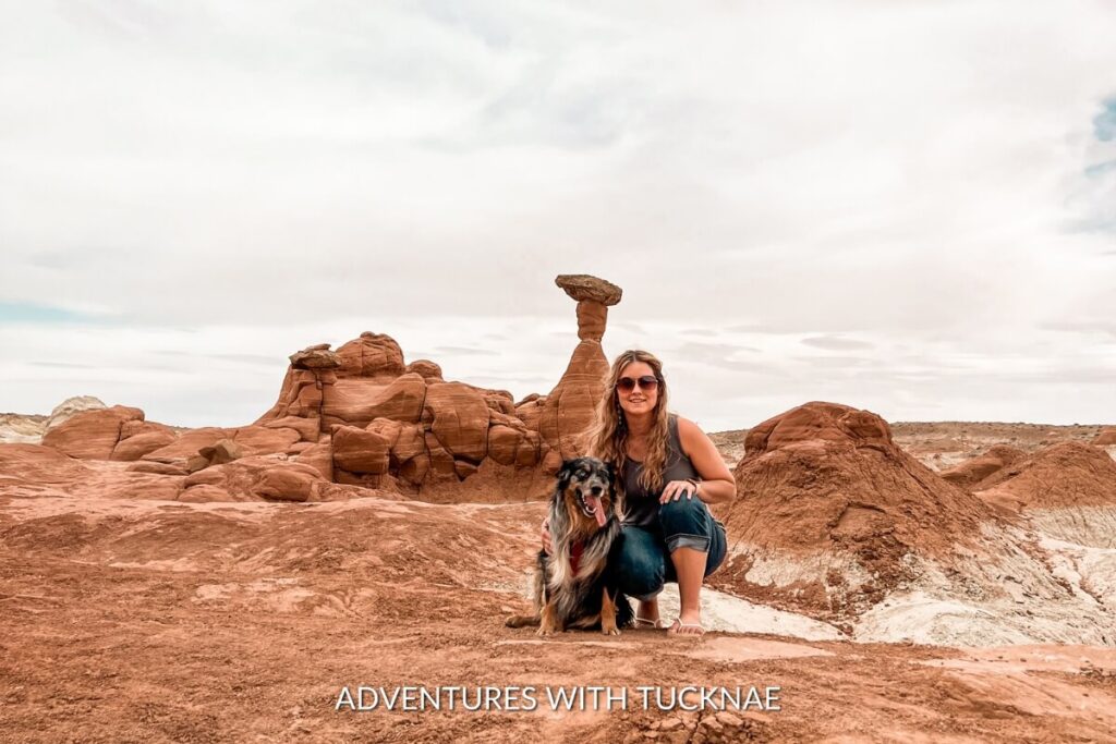 A hiker and their dog pose near balanced rock formations during the Toadstool Hoodoos Hike, an instagrammable geological wonder with a stark contrast of red and white layers in Utah.