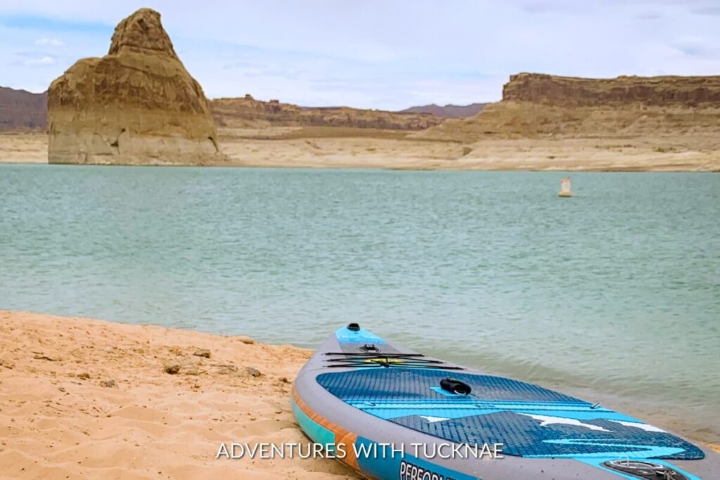 Paddleboard rests on the sandy shore of Lone Rock Beach at Lake Powell, with the iconic Lone Rock formation in the background, a serene and instagrammable spot in Utah.
