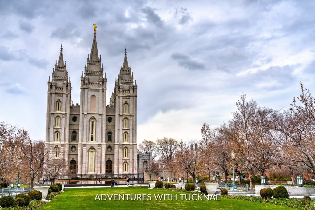 The majestic Salt Lake Temple stands with its striking spires against a dramatic sky, surrounded by manicured grounds, a historic and instagrammable landmark in Utah.