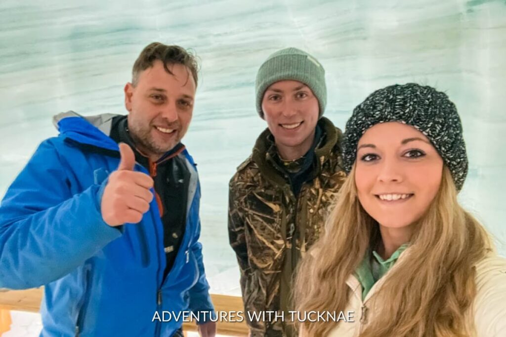 Group selfie inside the Into the Glacier ice tunnel, with a man in a blue jacket giving a thumbs up, flanked by a man in camouflage and a woman in a black beanie.