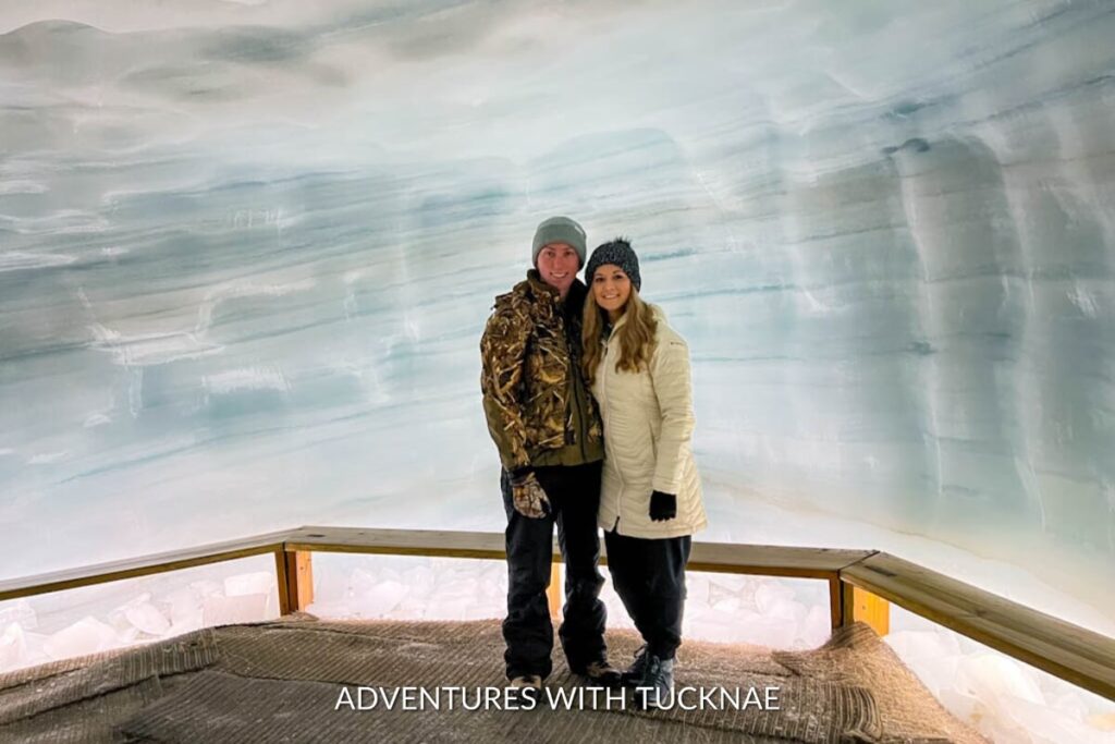 Smiling couple posing in the clear blue ice cave at Into the Glacier, showcasing the smooth glacial walls and safe viewing platform.