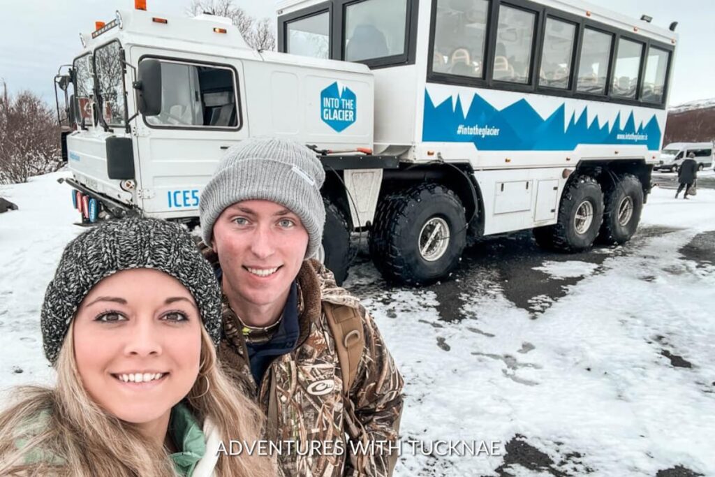 Tourists taking a selfie in front of the Into the Glacier ice explorer truck, with the vehicle's branding and snowy landscape in the background.
