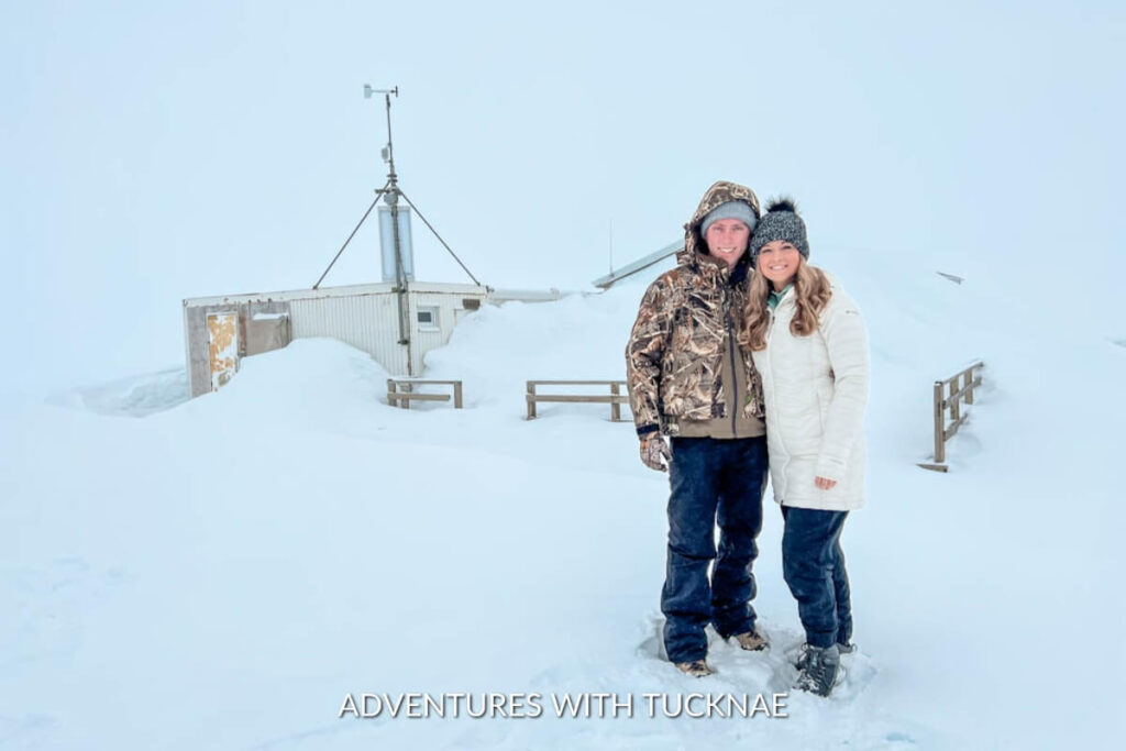 Happy couple standing in front of a snow-covered building at Into the Glacier, with visibility reduced due to the surrounding whiteout conditions.