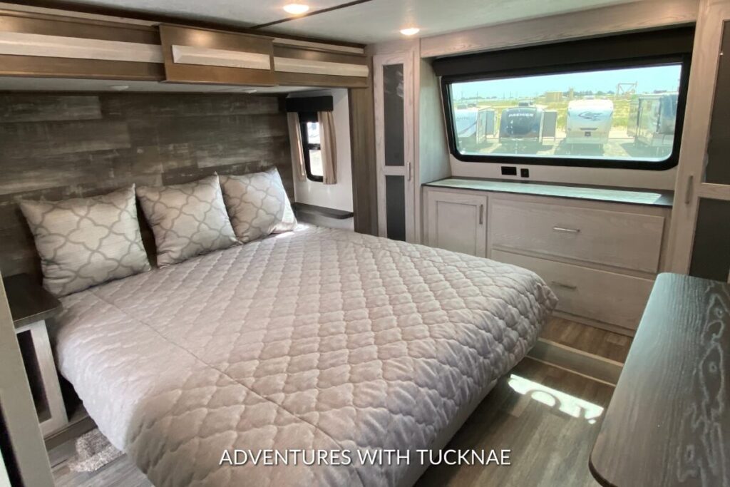 Master bedroom in a Keystone Montana RV featuring a queen-sized bed with decorative pillows and overhead storage cabinets.