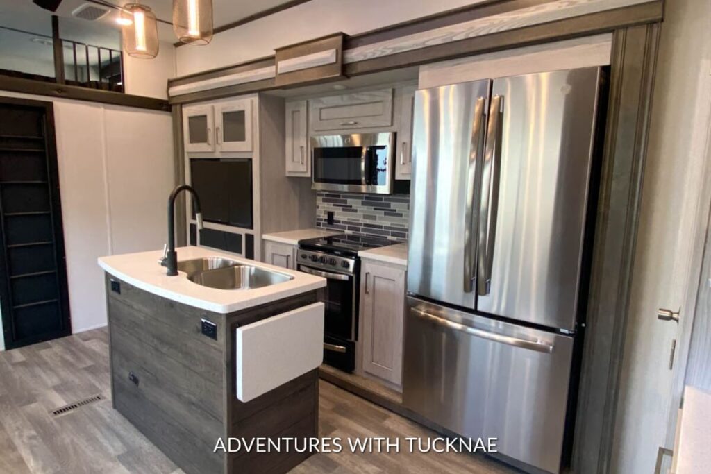 Modern RV kitchen with stainless steel refrigerator, gas stove, and wooden cabinetry in a Keystone Montana High Country RV.