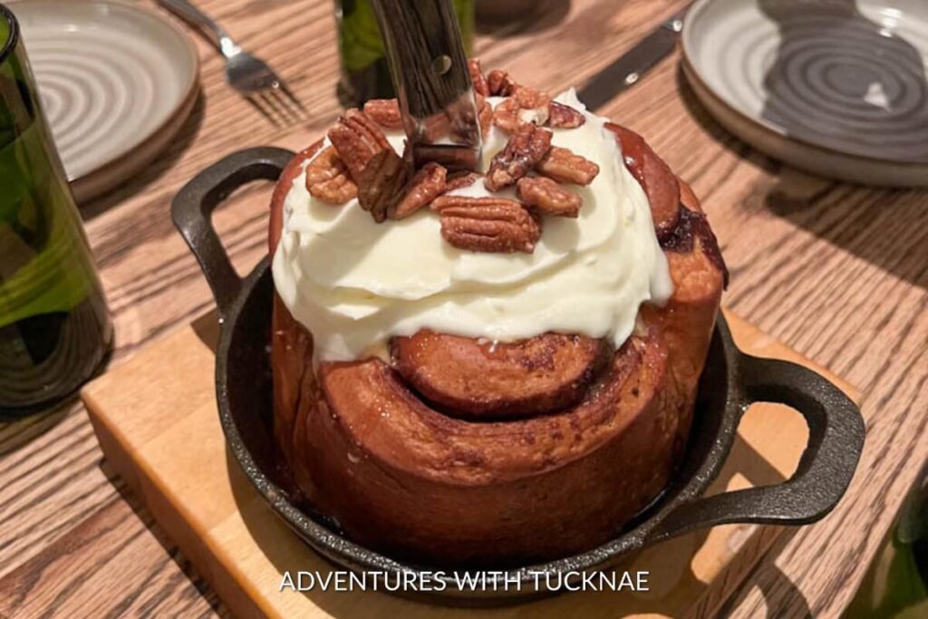 A gigantic cinnamon roll topped with creamy frosting and crunchy pecans, served in a cast iron skillet, ready for indulgence in Las Vegas.