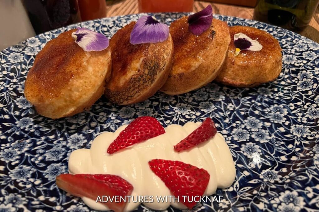 Golden-brown brioche doughnuts adorned with purple edible flowers, accompanied by a dollop of cream and fresh strawberries, a delightful dessert in Las Vegas.