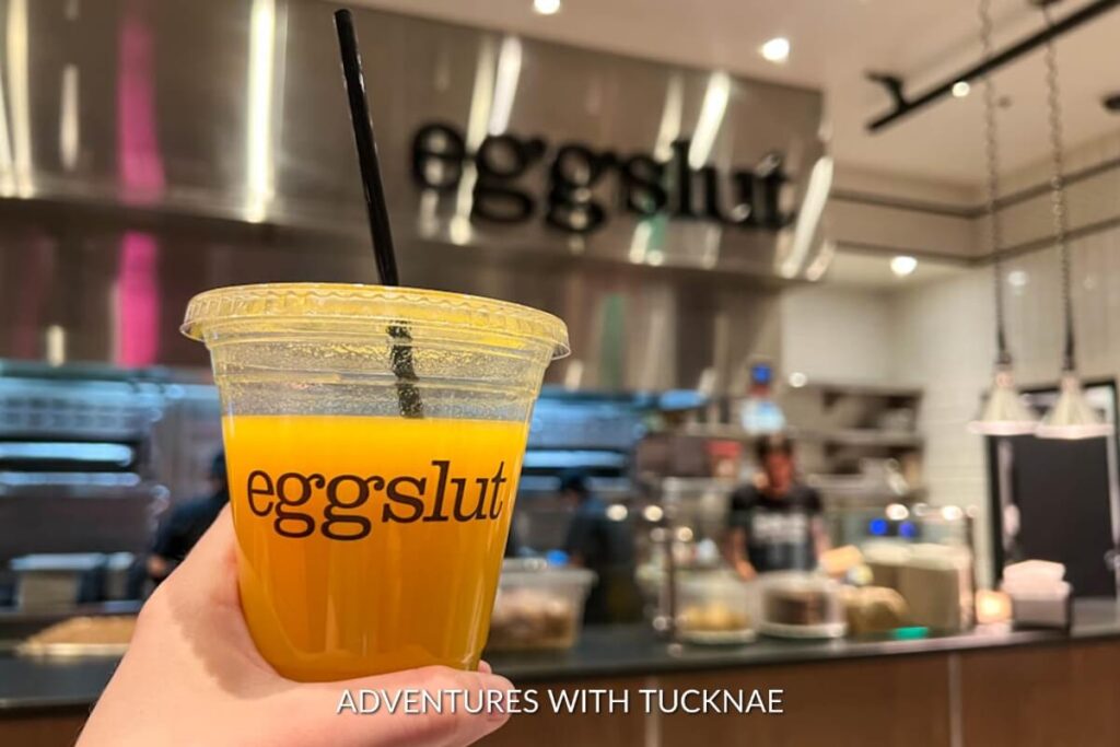 A glass of fresh orange juice with a black straw, branded with 'Eggslut', a popular breakfast spot in Las Vegas.
