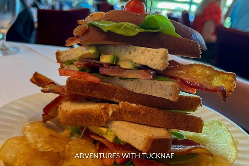 A towering club sandwich with bacon, lettuce, and tomato, paired with crispy potato chips, a staple lunch item in Las Vegas.