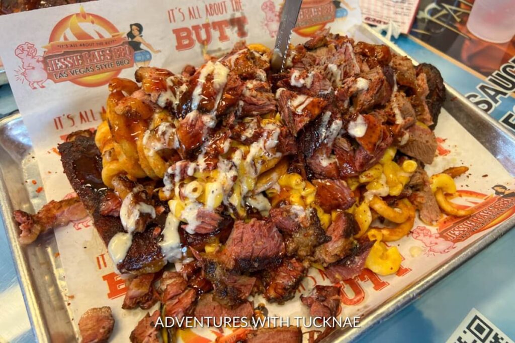 A mouth-watering heap of barbecue pulled pork and macaroni on a bed of curly fries, drizzled with sauce and served on a branded tray, epitomizing Las Vegas BBQ style.