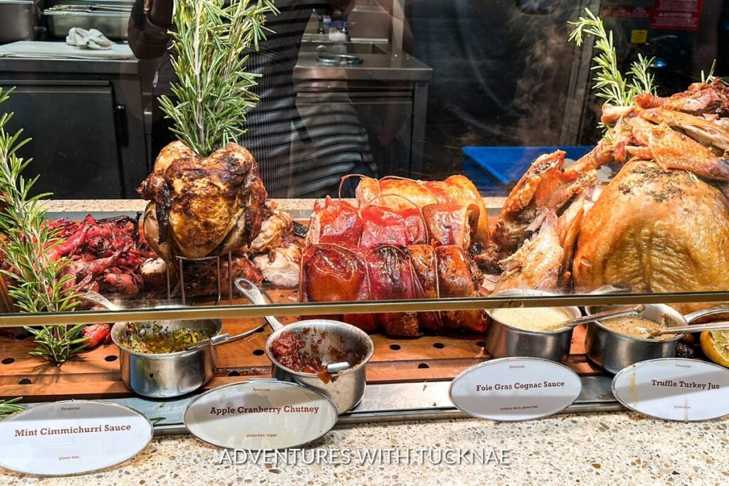 A diverse array of roasted meats including chicken and porchetta, displayed with accompanying sauces like mint chimichurri and apple cranberry chutney, a carnivore's delight at the Bacchanal Buffet in Las Vegas.