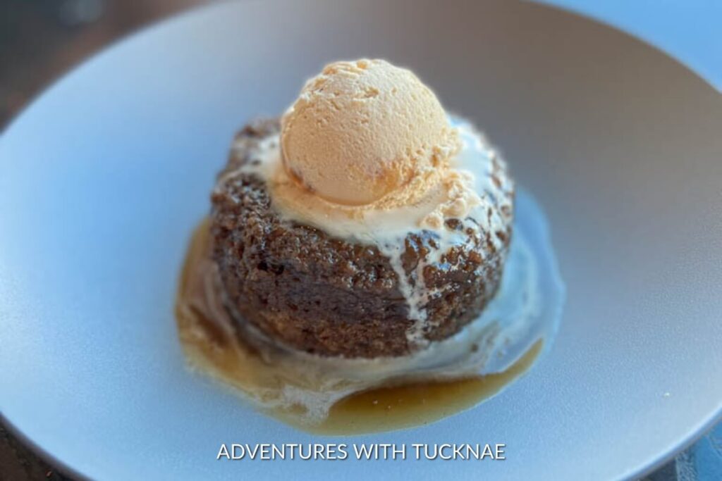 A delectable sticky toffee pudding topped with a scoop of vanilla ice cream, drizzled with caramel sauce on a white plate, a sweet treat from a Las Vegas restaurant.