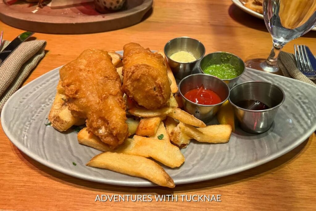 Crispy beer-battered fish laying atop a bed of fries, served with a trio of dipping sauces, a Las Vegas take on the classic British pub fare.
