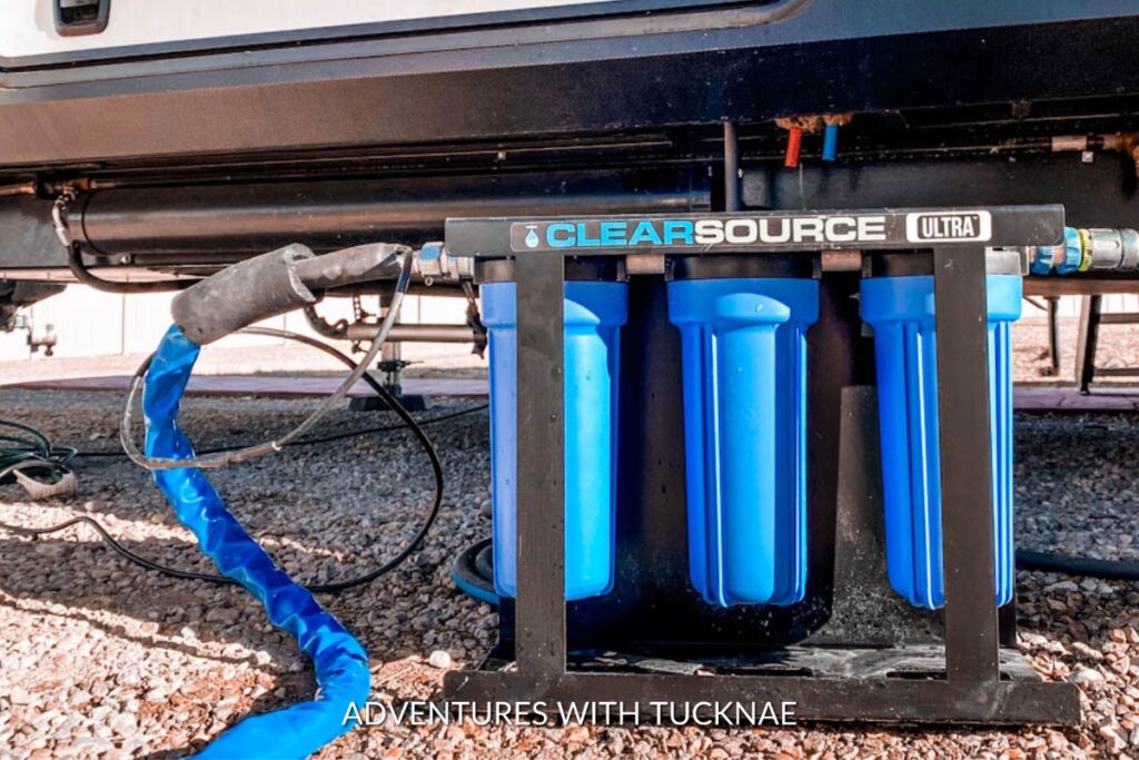 A Clearsource Ultra water filtration system installed under an RV, with blue hoses connected, ensuring clean water supply.