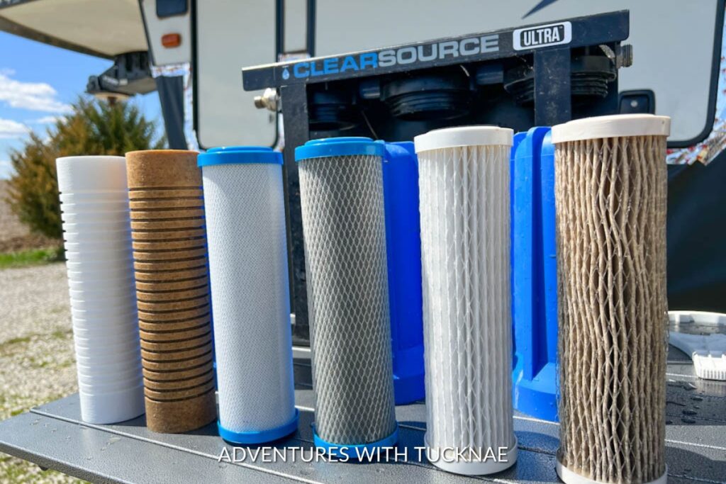 Various used water filters displayed in front of an RV, showcasing different stages of wear and types of filters for clear water system maintenance