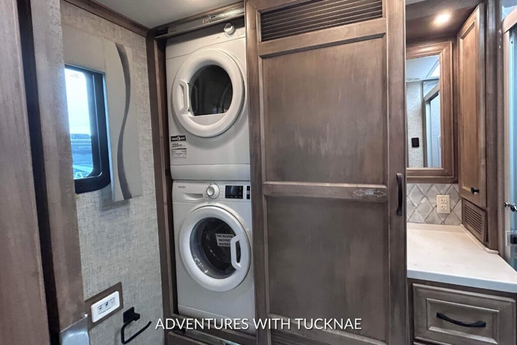 A space-saving RV laundry solution featuring a white stacked washer and dryer set within a wooden cabinet structure in an RV.