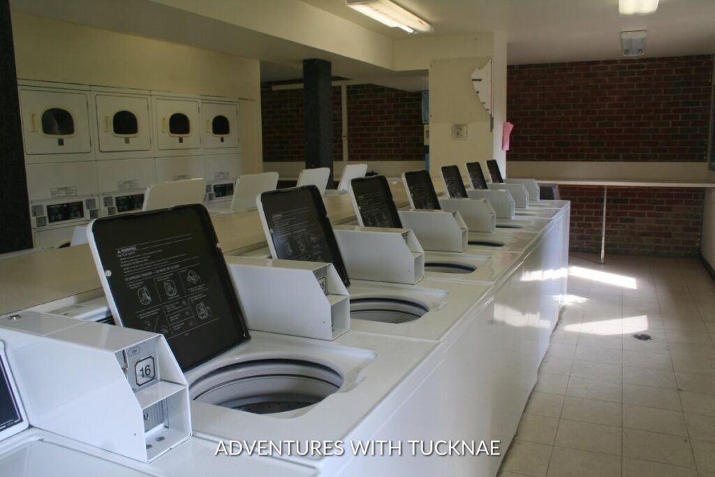 An array of white top-loading washing machines in a clean laundry room with brick walls, a common sight for communal RV laundry facilities.