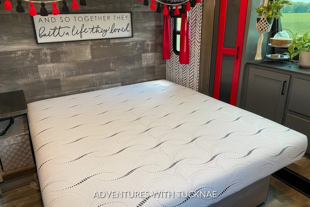New white RV mattress laid out on a wooden bed frame with a decorative sign reading 'And so together they built a life they loved' above in a cozy interior.