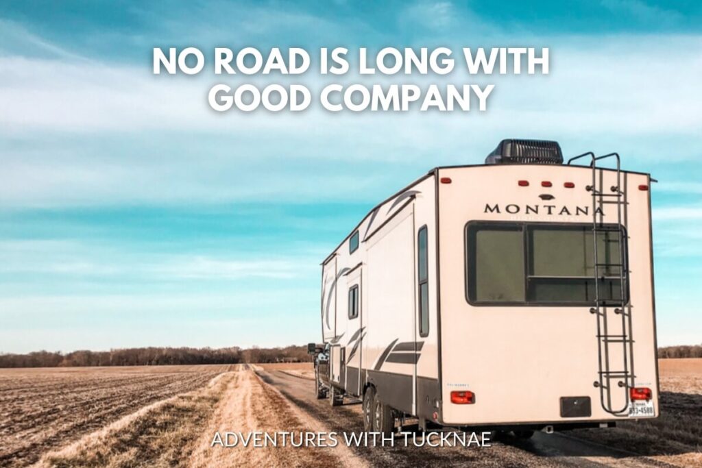 Rear view of a stationary RV on a dirt road through farmland with the quote 'No road is long with good company.'