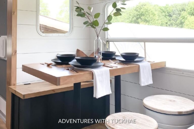 A stylishly simple RV dining setup with a wooden tabletop on black legs, contrasting with elegant blue dinnerware.