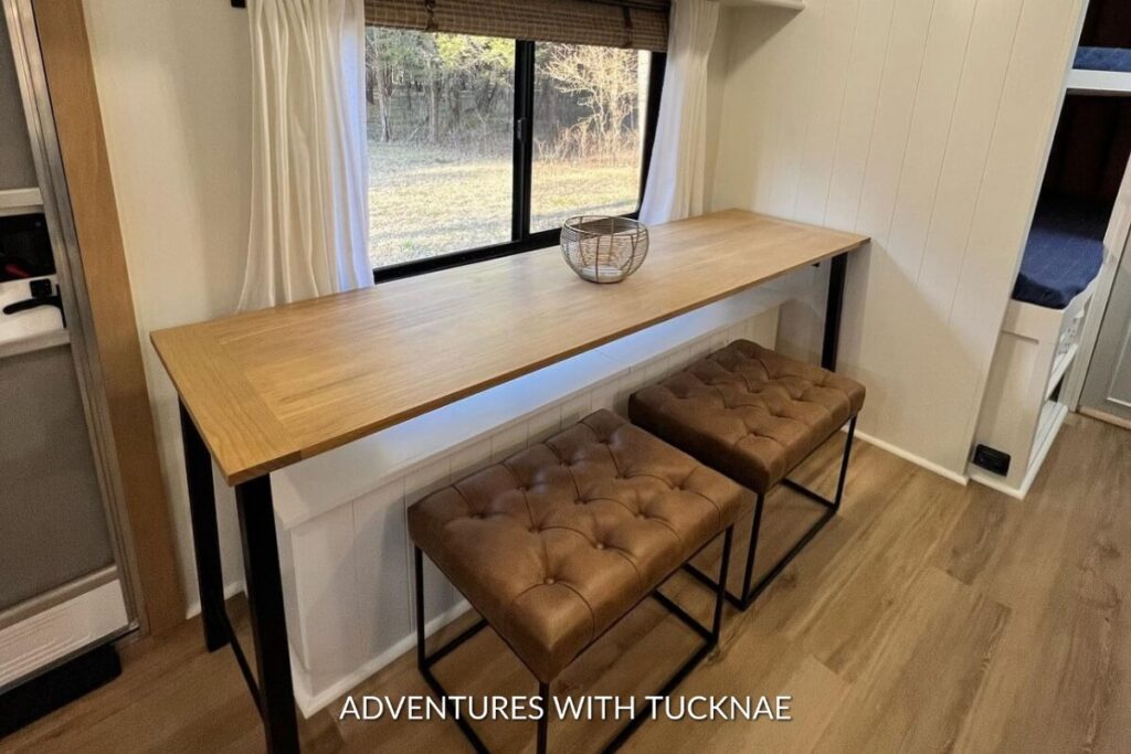 An inviting RV dining area with a rustic wooden table, tufted benches, and a scenic window view, perfect for a meal on the road.