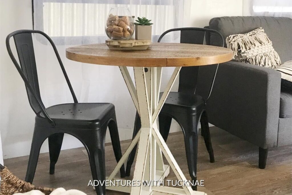 Unique RV table with a round wooden top and vintage white base, paired with black metal chairs for a distinctive RV dining experience.