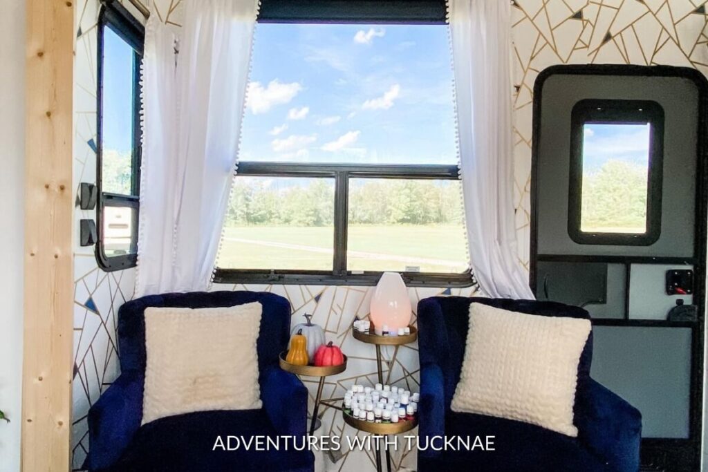 Elegant RV sitting area with a geometric golden wallpaper, featuring plush blue chairs and a small round table with a minimalist decor.