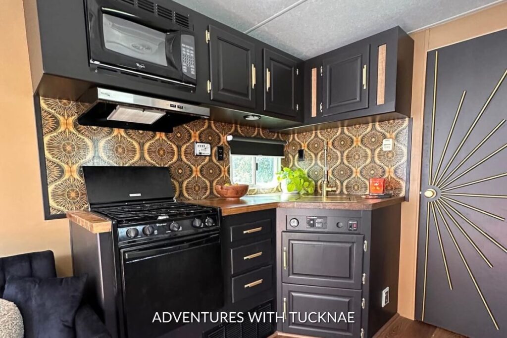 RV kitchen highlighted by a sunburst pattern wallpaper in gold and brown tones, coordinating with dark cabinets and a natural wood countertop.