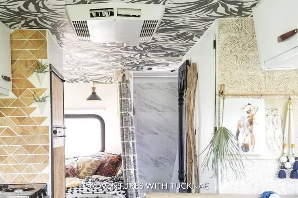 RV interior featuring a ceiling covered in a striking black and white abstract wallpaper, complemented by a herringbone wood floor.