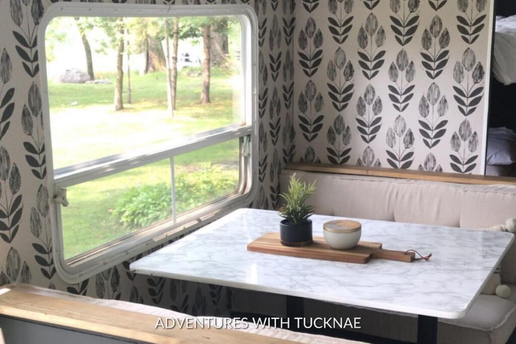 RV dining area set against a leafy black and white wallpaper, offering a tranquil view through the window, with a marble-patterned table set for a cozy meal.