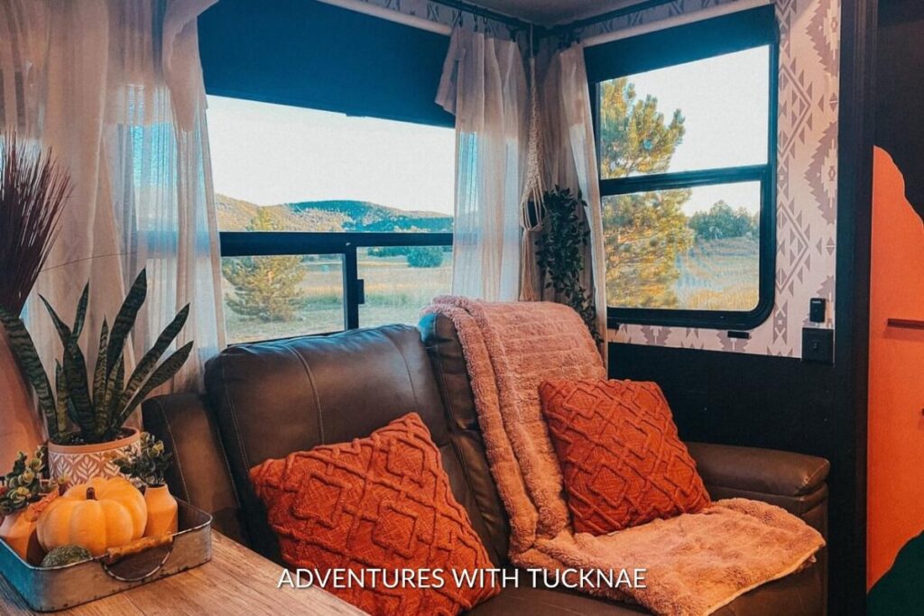 Inviting RV lounge area with rich terracotta-hued throw pillows and blankets against a window, enhanced by a Southwestern-patterned wallpaper.