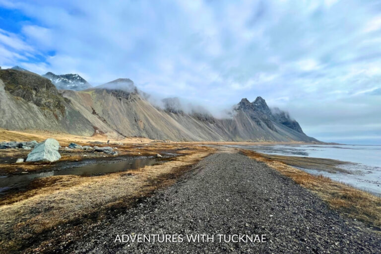 A gravel path leading towards towering misty mountains and a serene coastline, illustrating the remote beauty of Iceland's landscapes.