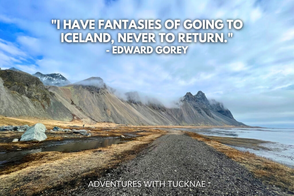 A gravel path leading towards towering misty mountains and a serene coastline, illustrating the remote beauty of Iceland's landscapes with the quote, "I have fantasies of going to Iceland, never to return." by Edward Gorey.