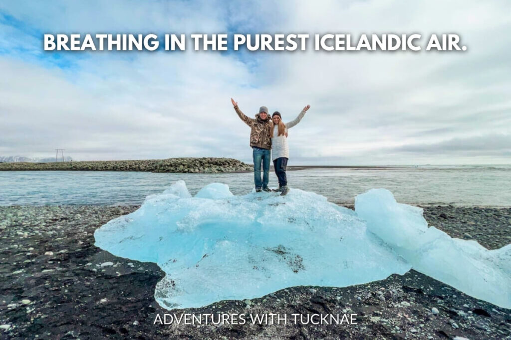 Two individuals on an ice floe with arms raised in triumph, breathing in the pure Icelandic air, with a vast icy landscape in the background.