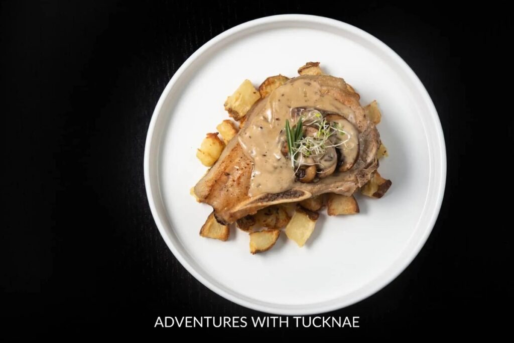 Instant Pot Pork Chops: A white plate showcasing golden-brown Instant Pot pork chops over a bed of roasted potatoes, finished with a creamy mushroom sauce.