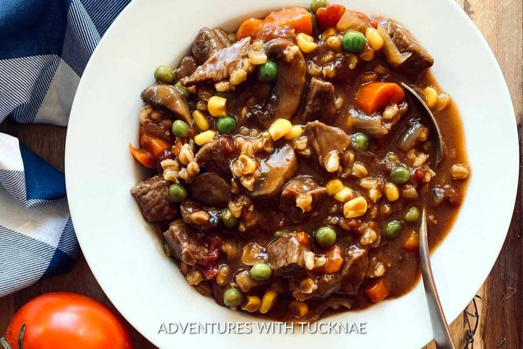 Instant Pot Vegetable Beef Soup: Hearty Instant Pot vegetable beef soup in a white bowl, brimming with beef chunks, peas, corn, carrots, and gravy.