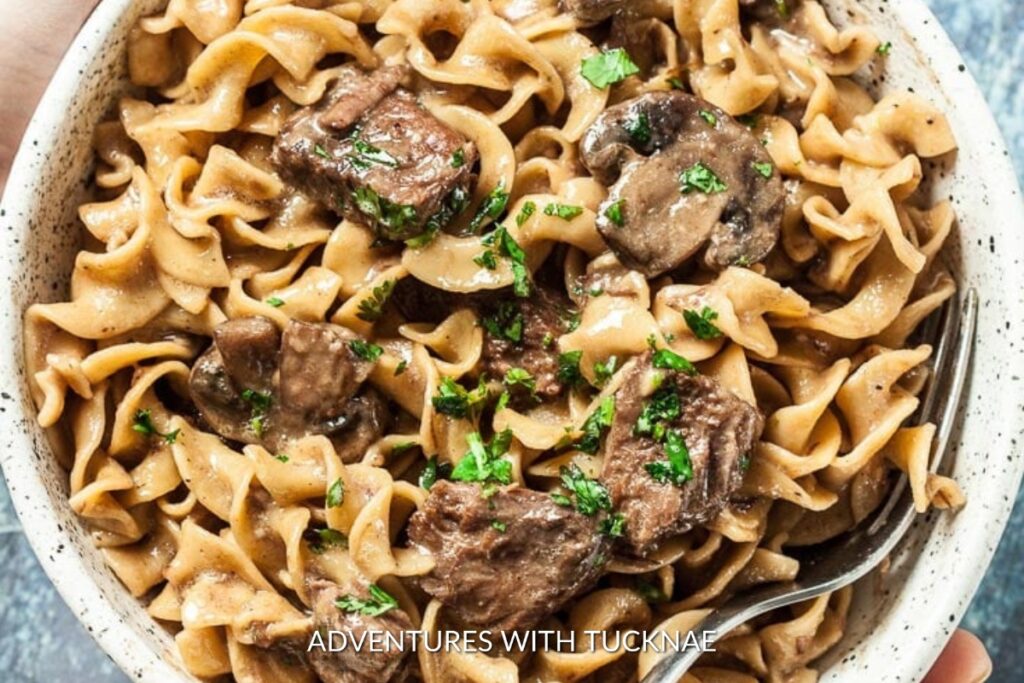 Instant Pot Beef Stroganoff: Creamy Instant Pot beef stroganoff served in a speckled bowl, with tender beef slices and mushrooms over noodles, garnished with parsley.