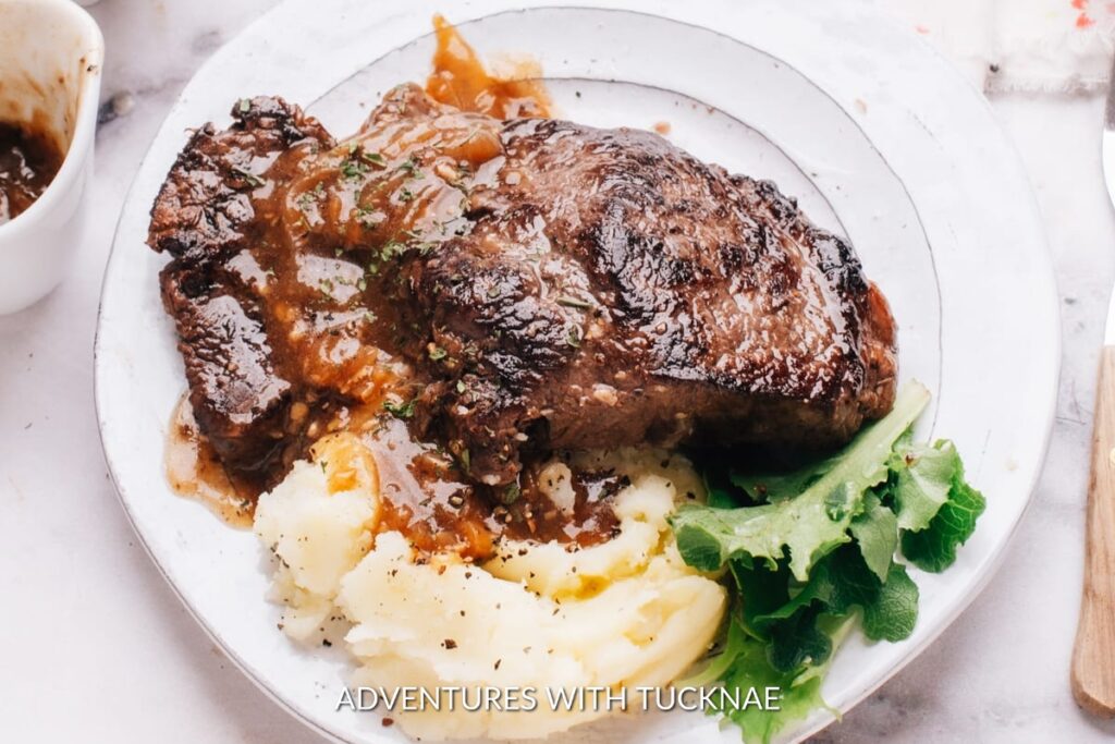 A plate of succulent Instant Pot Steak with a rich gravy, paired with mashed potatoes and salad, a luxurious camping meal.