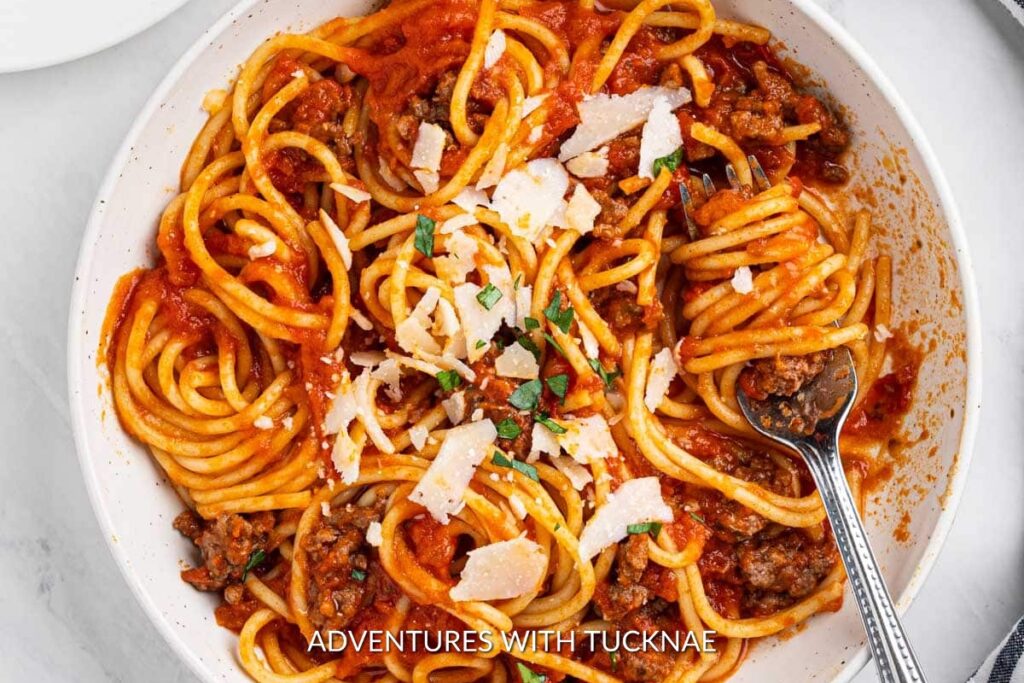 Instant Pot Spaghetti: Twirls of Instant Pot spaghetti in a tangy tomato sauce with ground beef, topped with parmesan cheese and fresh herbs, on a white plate.