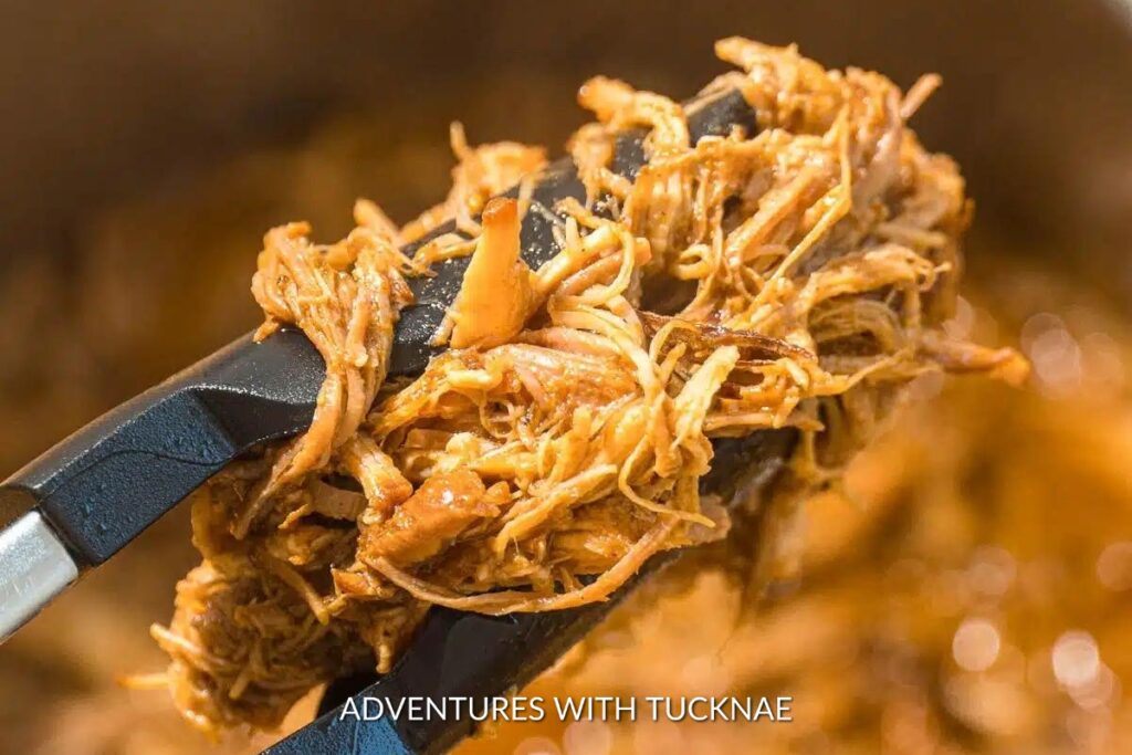 Instant Pot BBQ Pulled Pork: Fork-tender Instant Pot BBQ pulled pork held with tongs, showcasing the juicy, barbeque-coated strands perfect for sandwiches.