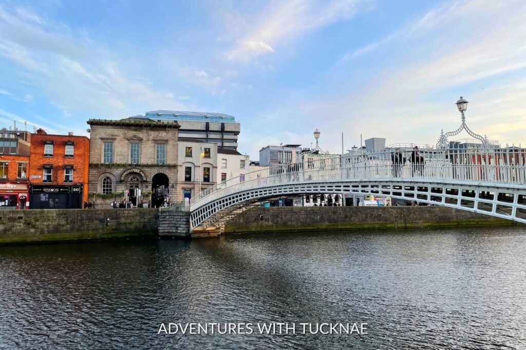 The iconic Ha’Penny Bridge over the River Liffey, a historic structure and Instagrammable spot in Dublin, with pedestrians crossing in the evening light.