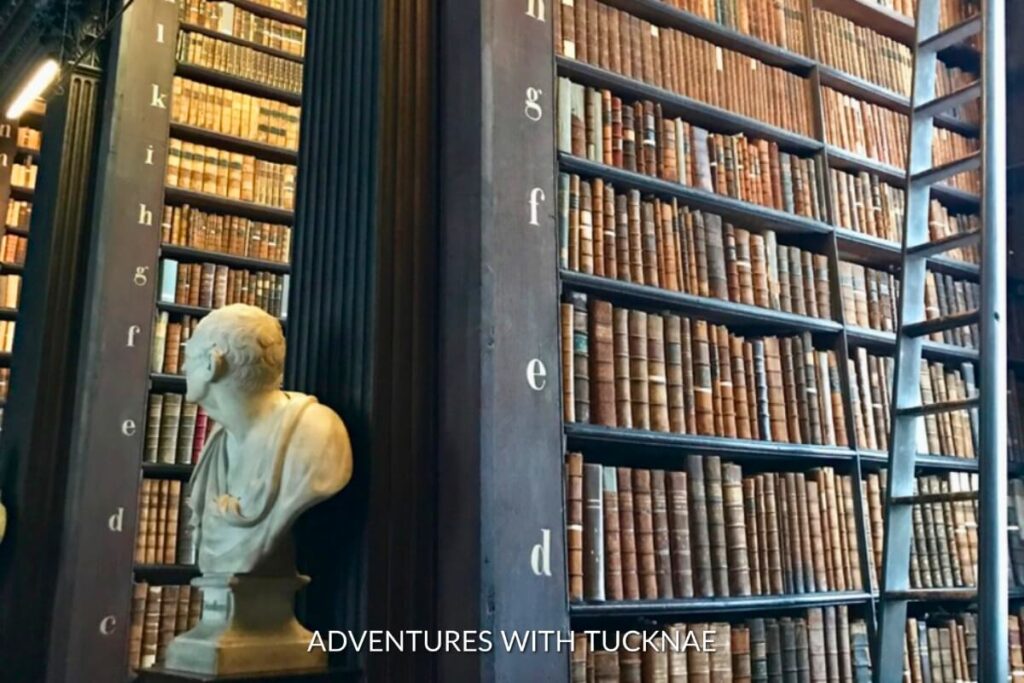 A marble bust and towering ancient bookshelves inside the Trinity College Library, representing Dublin's rich literary history and Instagram-worthy locations.
