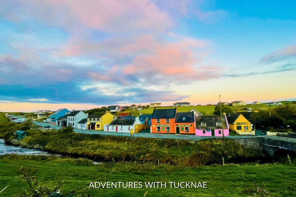 A vibrant sunset paints the sky over the quaint village of Doolin, Ireland, an Instagrammer's dream with its colorful houses along the serene river.
